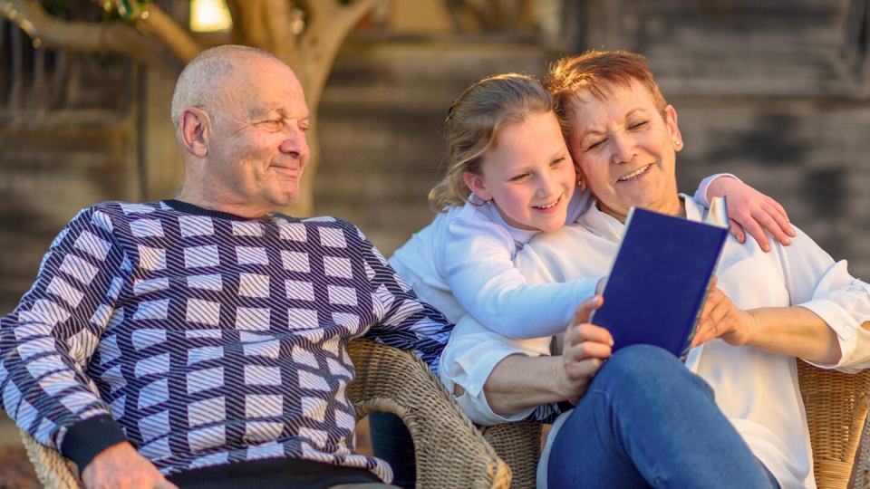 Senior couple reading a book with granddaughter in the sun