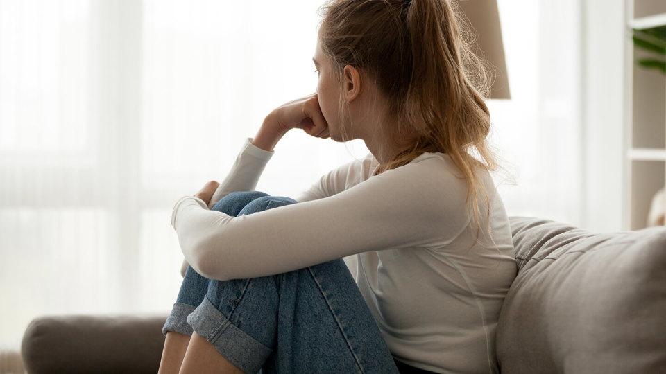 Side view young woman looking away at window sitting on couch at home. Frustrated confused female feels unhappy problem in personal life quarrel break up with boyfriend or unexpected pregnancy concept