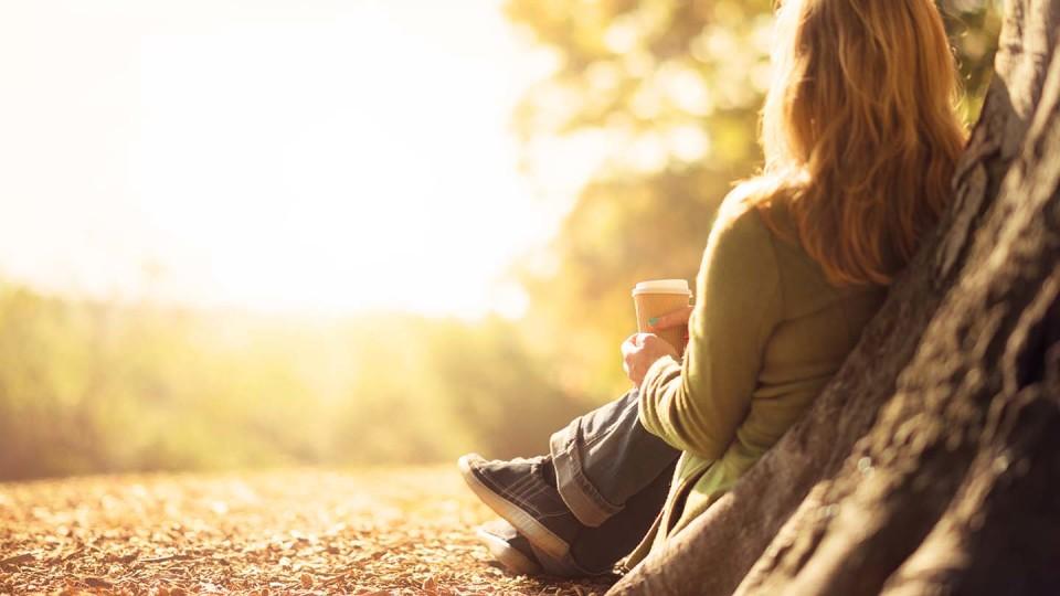 Woman drinking coffee against tree - from behind