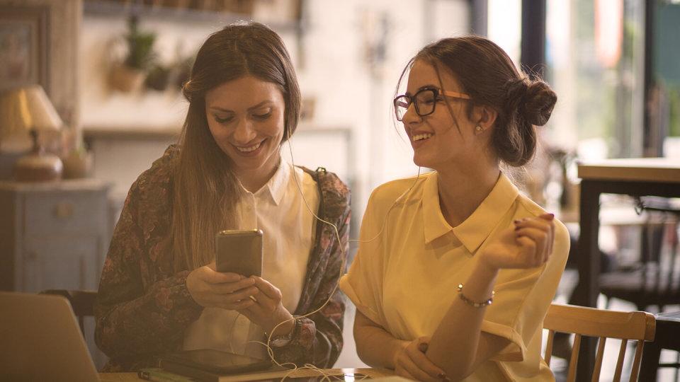 Two friends sharing headphones and laughing