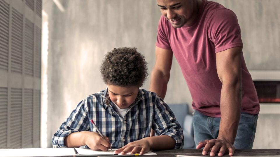 Young son sat at desk with father looking over his shoulder