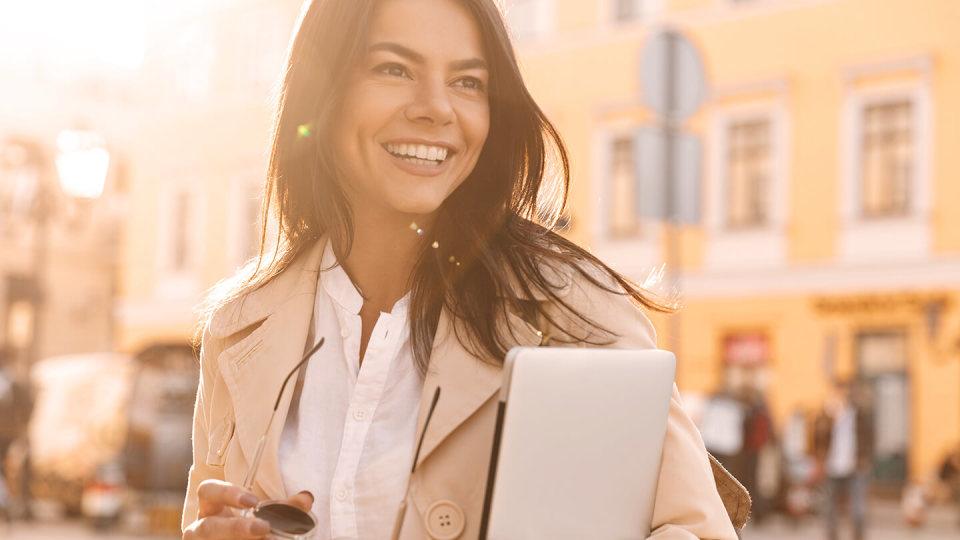 Smiling woman holding laptop in the street