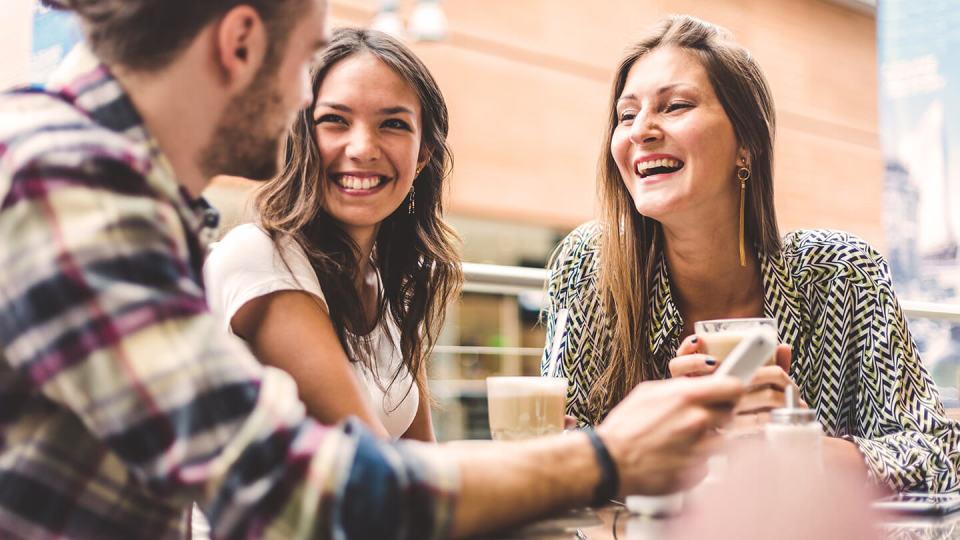 Two women laughing with their friend holding a phone