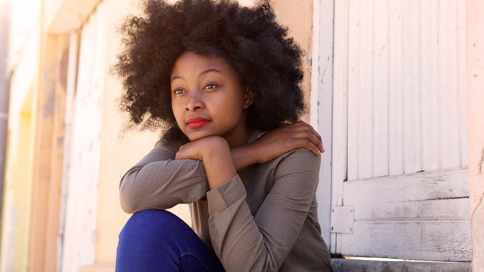 Young woman sitting outside her front door gazing into the distance